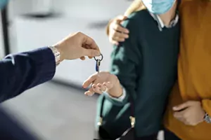 Stock imagery showing an off-screen person handing keys to two people standing together, one with their arms around another.