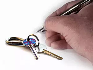 Stock image showing keys and a hand holding a fountain pen ready to sign.