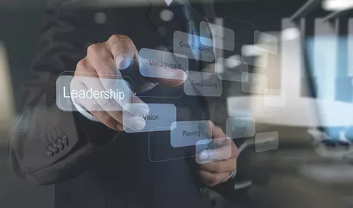 Stock image showing a hand pointing towards a digital screen from behind the screen. The screen shows a diagram that has the words leadership, management, vision, construction, responsibility, and planning over rectangular buttons